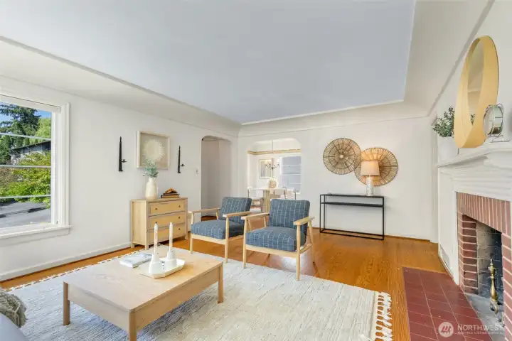 Spacious, light-filled living room with coved ceilings, original millwork, wood-burning fireplace.