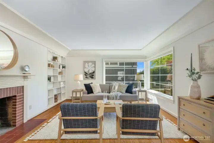 Spacious, light-filled living room with coved ceilings, original millwork, wood-burning fireplace.