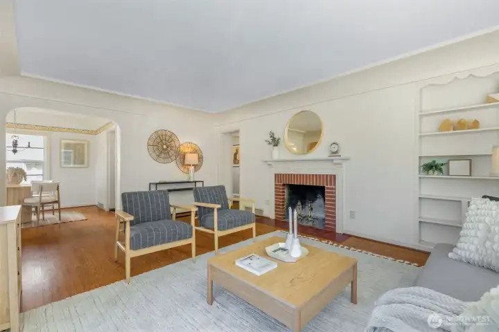 Spacious, light-filled living room with coved ceilings, original millwork, wood-burning fireplace.