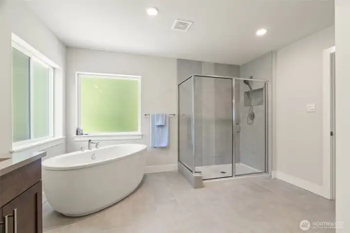 Indulge in spa-like luxury without leaving home. The stunning primary ensuite showcases a freestanding soaking tub, oversized walk-in glass shower with tile surround, and warm wood vanity cabinetry — every detail designed for relaxation and renewal.
