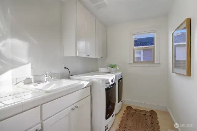 Upper floor utility room with sink, counter space for folding laundry and built-in cabinetry. Newer washer and dryer stay.