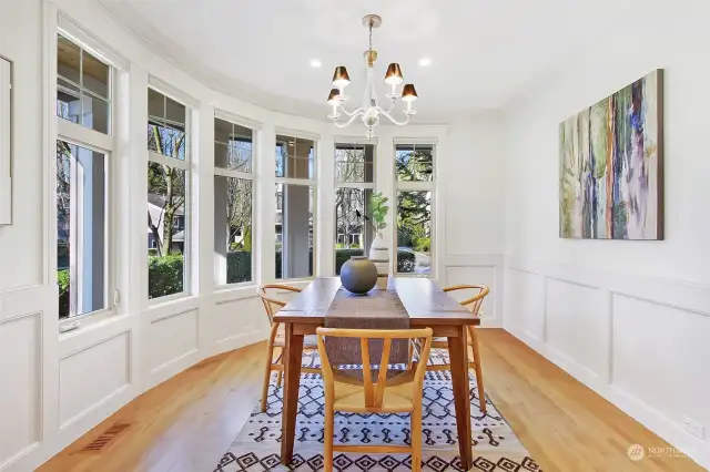 Architecturally interesting, rounded wall of windows is the other side of the charming wrap-around porch. Formal dining room with chandelier and warm oak floors will easily accommodate seating for 6-8.