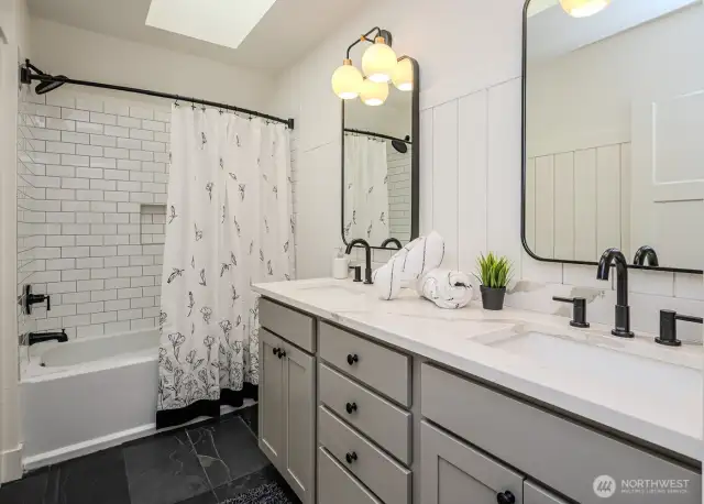 Upstairs full bath with dual quartz topped vanities, timeless tilework and private water closet.