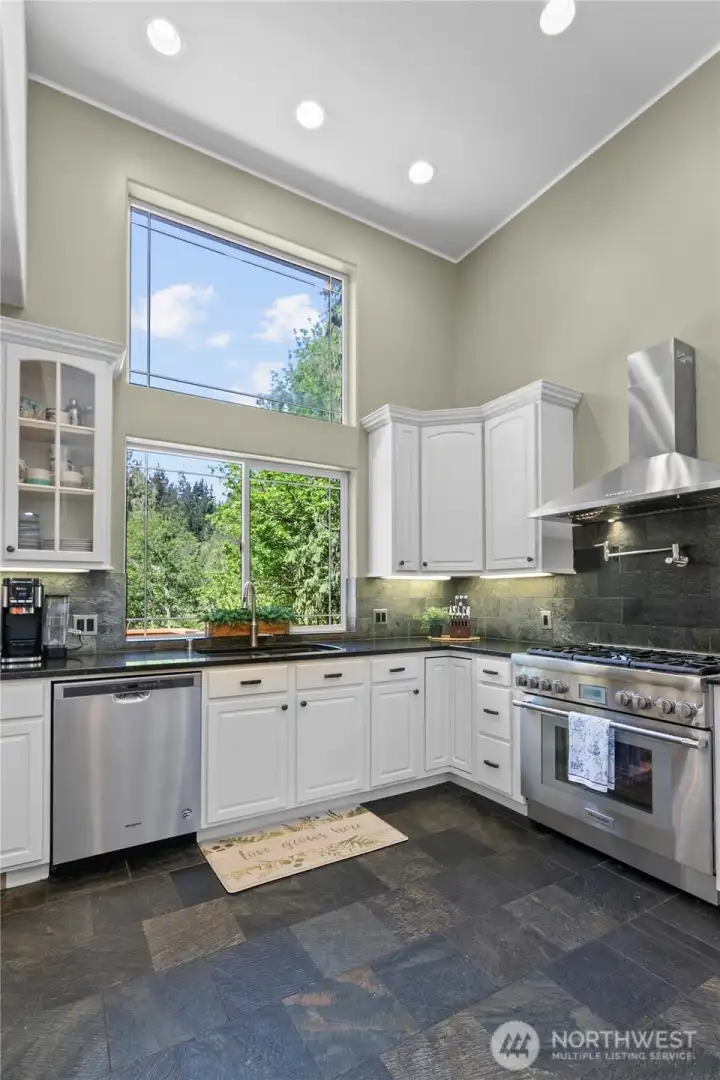 Chef-inspired kitchen with custom cabinetry, stone surfaces, stainless appliances, and dramatic ceiling height.