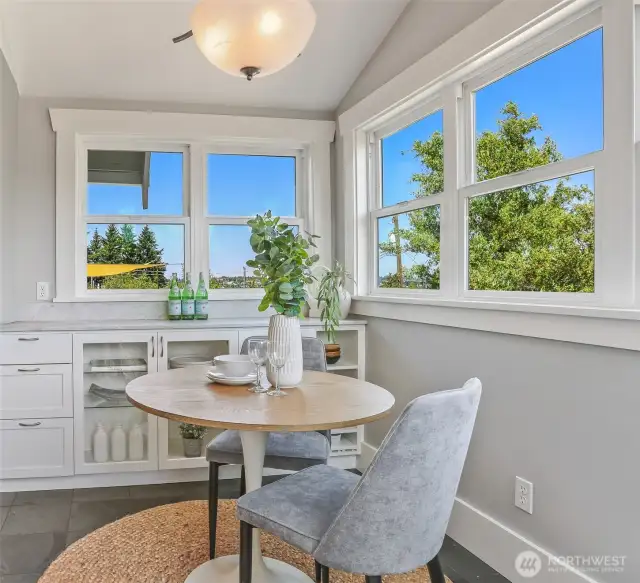 A bright and airy breakfast nook that lives like an atrium, featuring vaulted ceilings and walls of windows surrounded by greenery.