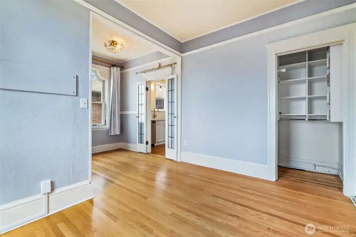 Hardwood flooring, soft lavender-gray walls, and windows with scenic water views create a cozy, sunlit space.