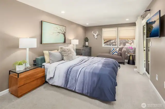 This modern primary bedroom offers a peaceful retreat with soft neutral tones, plush carpeting, and stylish decor. Features include a sleek barn door to the en-suite bath, frosted closet doors, a mounted TV, and sliding glass door to a private outdoor space—comfort meets contemporary charm.