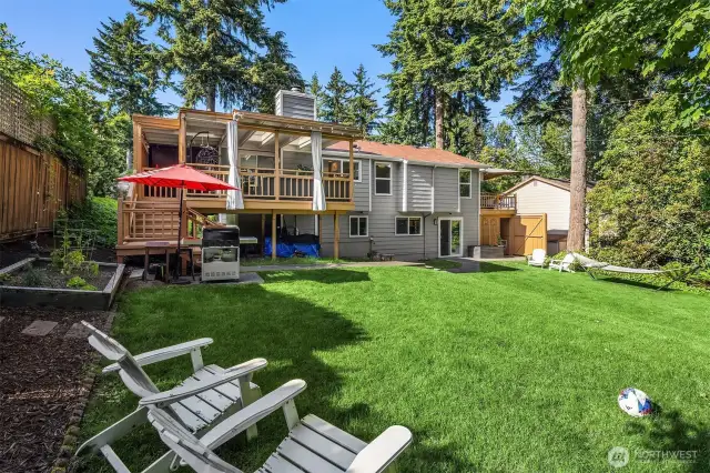The expansive backyard features a lush lawn, patio, and garden space framed by trees and full fencing—an entertainer’s dream and peaceful retreat rolled into one. The rear elevation of the home showcases its size and charm.