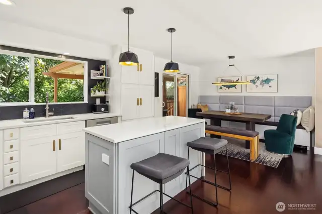 This stylish kitchen and dining area boasts modern pendant lighting, sleek quartz countertops, and custom cabinetry with brass hardware. The cozy built-in banquette and open layout create a perfect space for casual dining or entertaining, with easy access to the private outdoor deck.