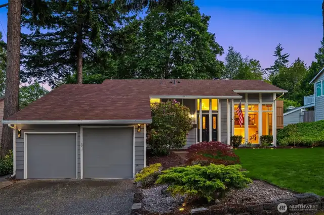 A wide driveway leads to a spacious two-car garage, while thoughtfully placed shrubs and seasonal blooms add warmth and character. The home's modern yet welcoming facade is bathed in natural light, setting the tone for the comfort and style that await inside.