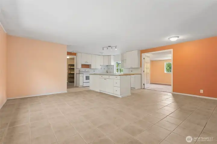 Step inside and you’re greeted by living room walls in autumn shades that balance cozy and bold, paired with a white-on-white kitchen that plays it clean. The island gives you a seat for coffee or chats with the cook, and French doors lead you into the next room with a little drama.