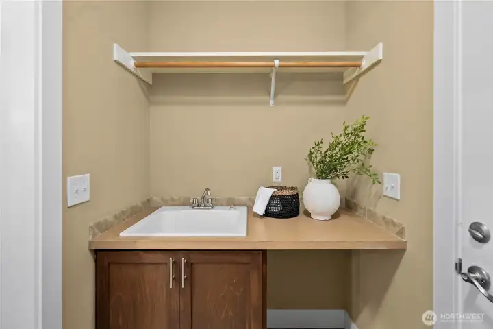 The laundry room features a laundry sink, cabinetry, a shelf, hanging rod and a folding station. Washer & dryer location is on the opposite side (not viewed in photo). The laundry room features a laundry sink, cabinetry, a shelf, hanging rod and a folding station. Washer & dryer location is on the opposite side (not viewed in photo).
