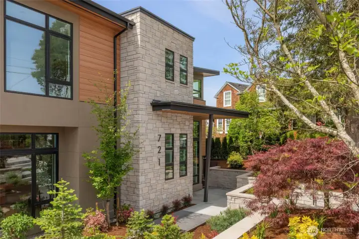 Entry is surrounded and supported by custom stone walls, stone pavers, corten steel planting beds, and covered porch with cedar ceiling