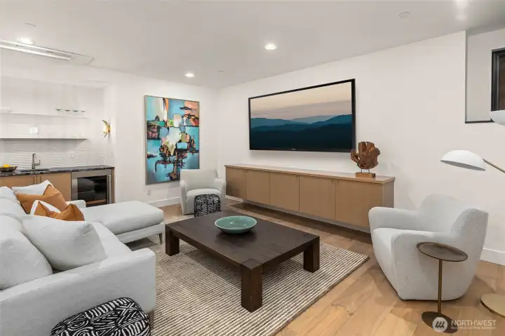 Lower level rec-room perfect for movie nights and game day. Supported by wet bar with custom oak cabinets, prep sink, undercounter Sub Zero beverage center, and full height tile backsplash with floating steel shelves