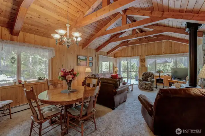 Spacious living and dining room boasts rustic beams, picture windows, cozy wood stove, and access to a wraparound deck overlooking the river.