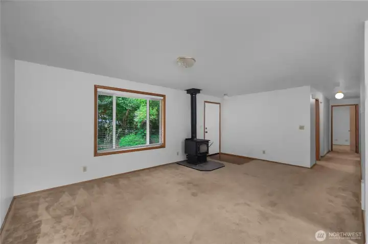 Spacious living area with large front window, wood stove, and freshly painted walls.