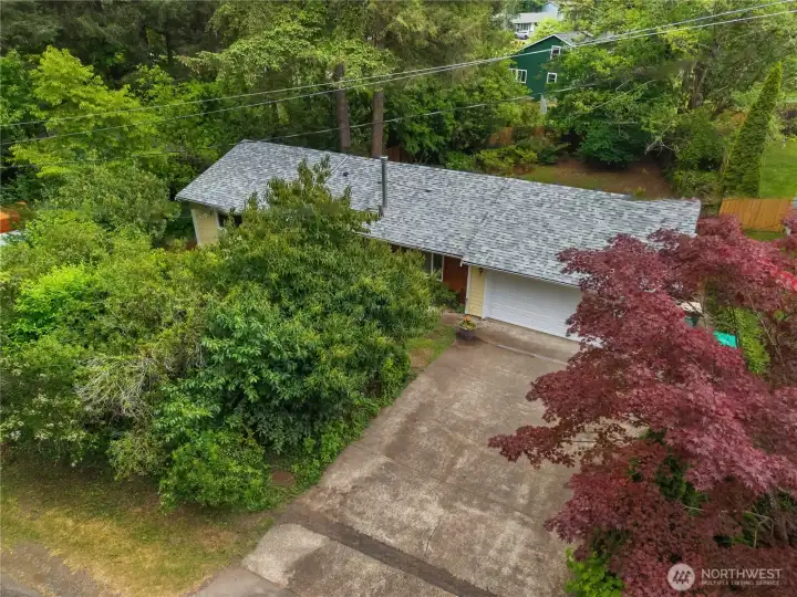 Aerial view of the home tucked into a mature, wooded lot with generous driveway parking.