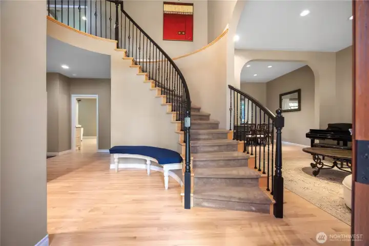 Grand entry foyer with soaring ceilings, updated wrought iron staircase railing, hardwood oak floors with white finish, and abundant natural light.