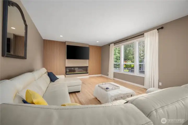 Spacious family room featuring updated electric fireplace, tall ceilings, open layout, and warm hardwood flooring perfect for entertaining.