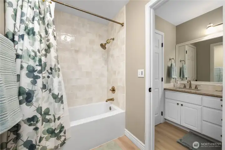 Stylish upstairs bathroom featuring Bluetooth speaker, LVP flooring, granite counters, and tiled surround.