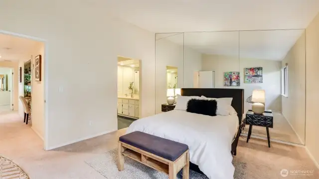 The primary bedroom features a stunning wall-to-wall mirror behind the bed, enhancing both the sense of space and natural light.