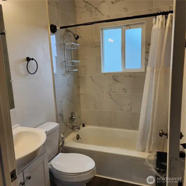 Full bath in hallway with newer upgrades, flooring, sink, tub, cabinets, marble tile and   window