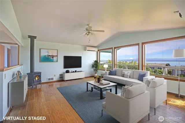 Living room w/ a wall of windows to soak in the views. The Lopi stove keeps you warm in the winter & the Mini Spit keeps you cool in the summer. Virtually staged.