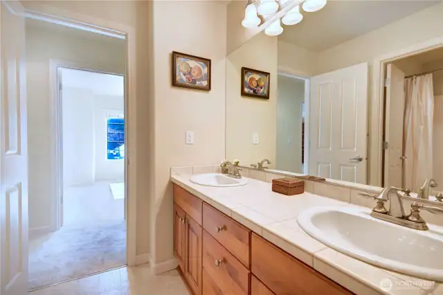 Upper floor bathroom in the hallway with tile flooring, double vanities, private tub and toilet.