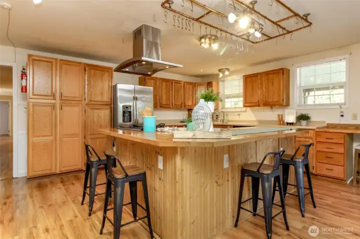 This kitchen is the heart of the home—warm, spacious, and designed for both everyday living and entertaining. Featuring an oversized island with bar seating, stainless steel appliances, and an abundance of cabinet storage, it’s perfect for meal prep or gathering with friends and family. Natural light pours in through large windows, highlighting the beautiful wood finishes and open layout. Whether you’re cooking up a feast or sipping your morning coffee, this inviting kitchen is sure to inspire.