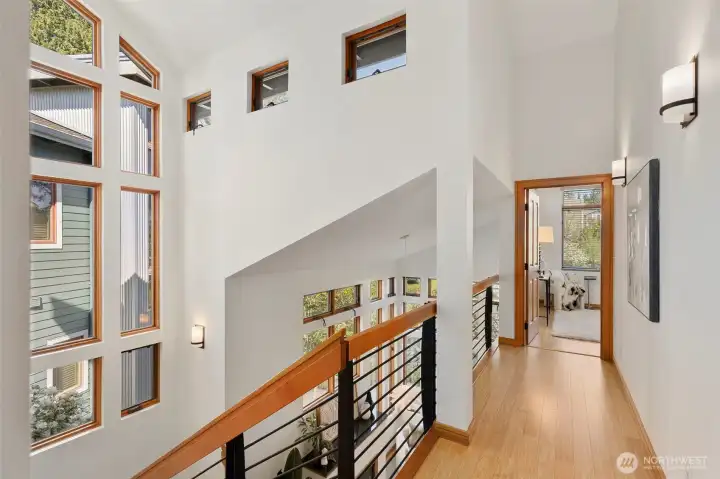 The upper-level hallway with bamboo floors, open railing overlooking the living room, and clerestory windows that keep the space bright.