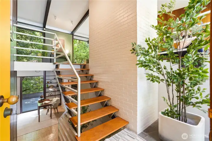 Dramatic floating staircase with rich mahogany treads anchors the entry, framed by a floor-to-ceiling white brick fireplace wall.