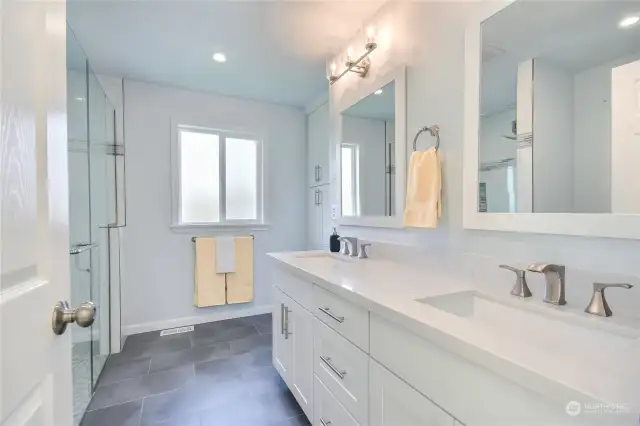 Gorgeous primary bathroom with heated tile floors, dual sink vanity with quartz counters, curbless, zero entry, tiled shower with bench, linen cabinets & toiled with heated seat.