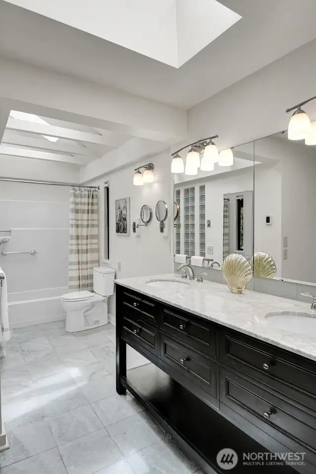 Primary bathroom in upper level features heated tile floors, vaulted ceilings, and skylights.
