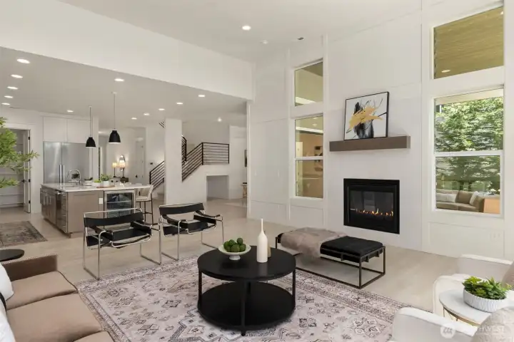 Another view of the bright and spacious great room/living room featuring a two-sided gas fireplace, large windows, and an open layout.