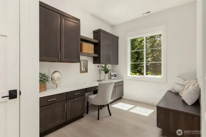Main-floor office featuring a built-in desk, cabinetry, and a built-in bench with pull-out storage drawers.