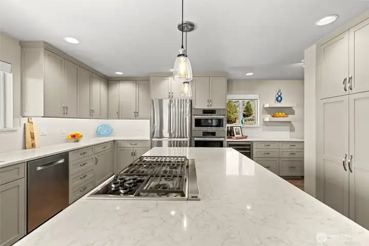 Bright kitchen with a 5 burner downvented propane cooktop, quartz countertops and abundant storage for added organization and functionality.