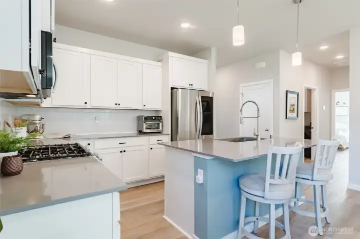 Quartz island with bar seating, farmhouse-style sink, and stainless dishwasher for functional prep space.