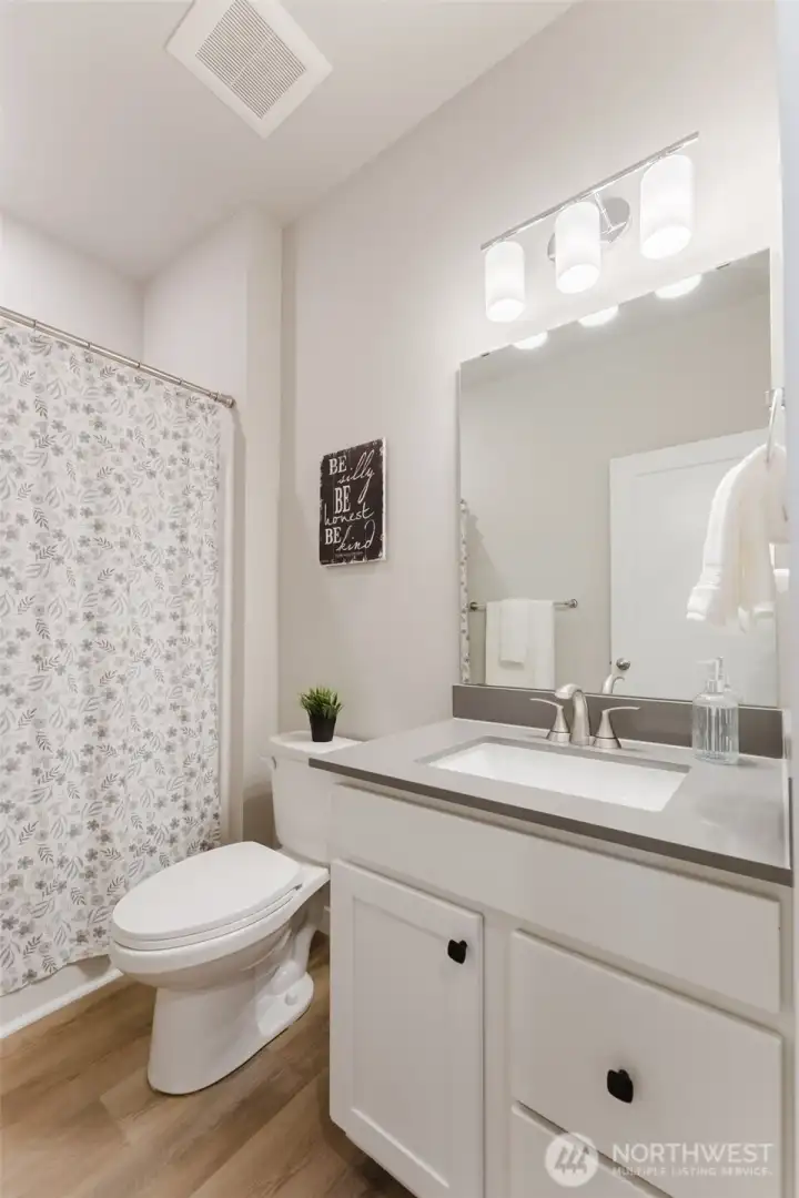 Bright full bathroom featuring quartz countertop, updated lighting, and neutral finishes, along with a tub/shower combo designed for easy everyday care.
