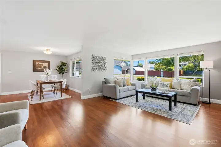 The spacious living room is filled with natural light from oversized picture windows. Warm hardwood floors add richness and timeless appeal.