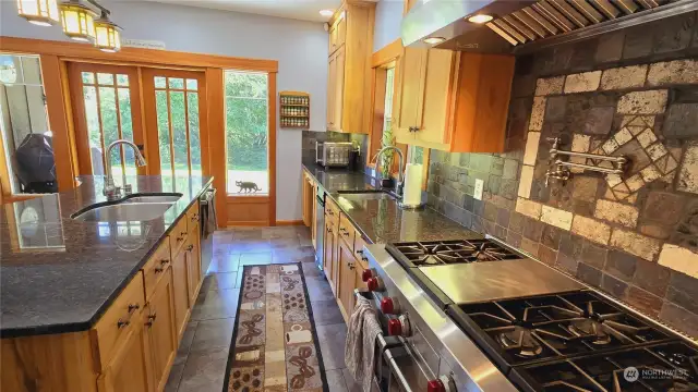 From the 6 burner + griddle range and double oven with pot filler spigot to the dual sinks, commercial grade hood fan and trash compactor this kitchen will thrill the most experienced chefs. Oh, and the covered deck houses the BBQ right out those wood clad french doors.