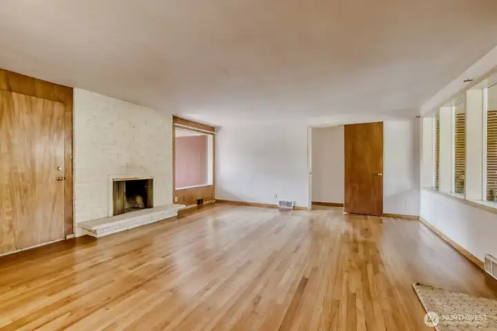 Living Room showcasing the original hardwood floor. These windows provide an abundance of natural light and makes this room happy and bright, even on gloomy Seattle days. Doorway at the far end leads to the hallway, 2 bedrooms, and the full bath.