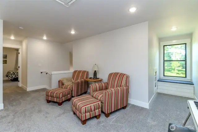Upper living room area with dormers on each side, built in shelving and seated windows.