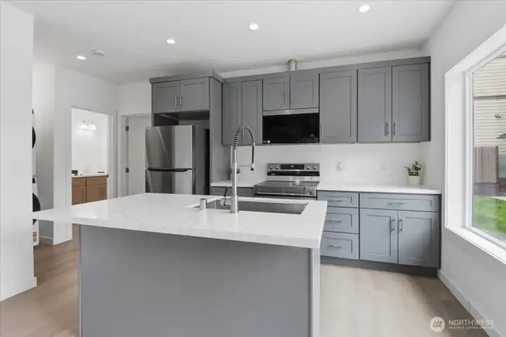 The large island creates a perfect eating space and boasts a quartz countertop with a deep, double stainless steel sink and a gooseneck faucet.