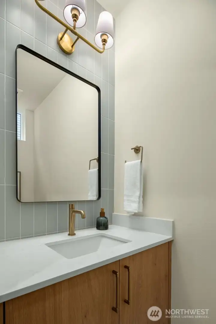 Stylish half-bath featuring a floating wood vanity, designer gold-rimmed mirror, and chic modern lighting.