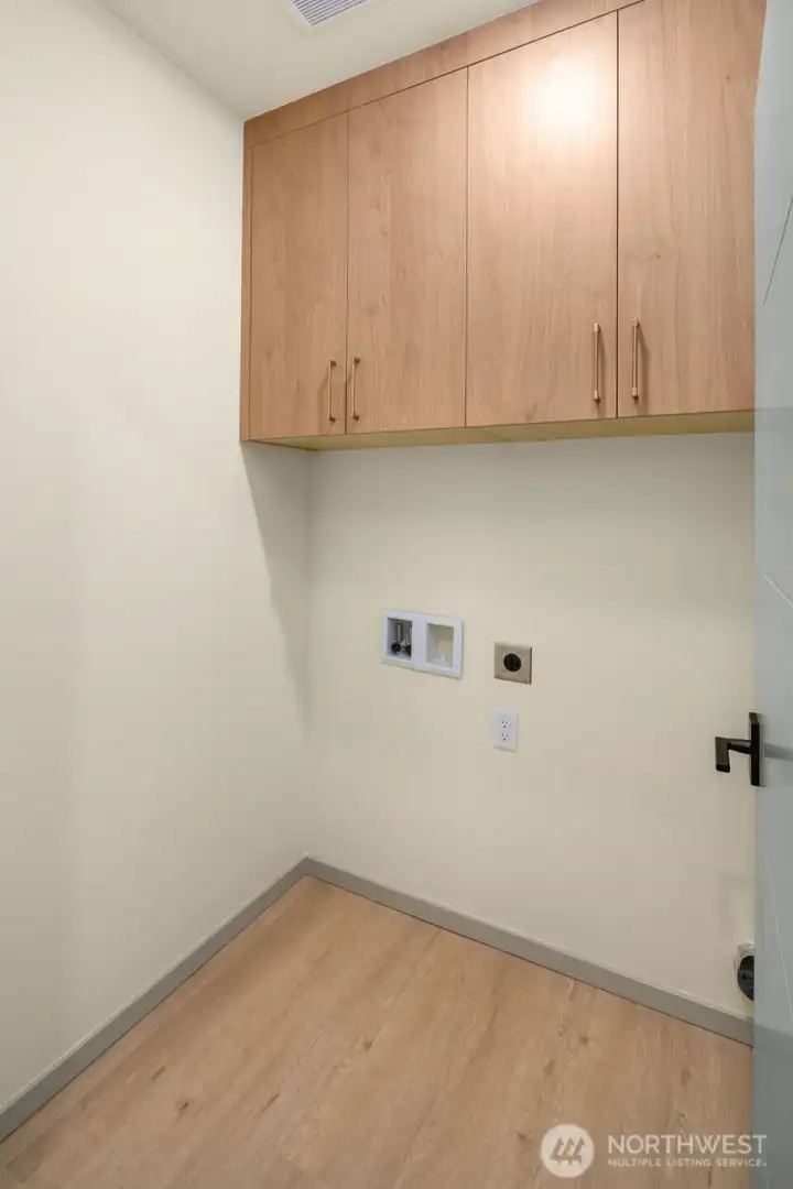 Functional utility room equipped with overhead storage cabinetry and dedicated hookups for a washer and dryer.