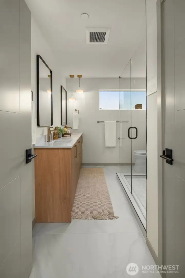 Modern bathroom vanity with warm wood tones, quartz countertops, and a large mirror reflecting the bright space.