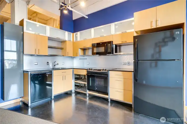 Sleek black and metal detailing pair beautifully with new stainless steel appliances—including a refrigerator, stove, and dishwasher—alongside warm wood cabinetry, granite countertops, and easy-care vinyl flooring. With generous storage, this kitchen is both stylish and highly functional.