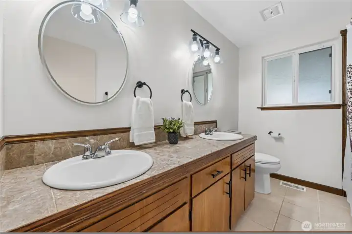 Hall bathroom with dual sinks, lots of cabinet storage, and a tub/shower combo.