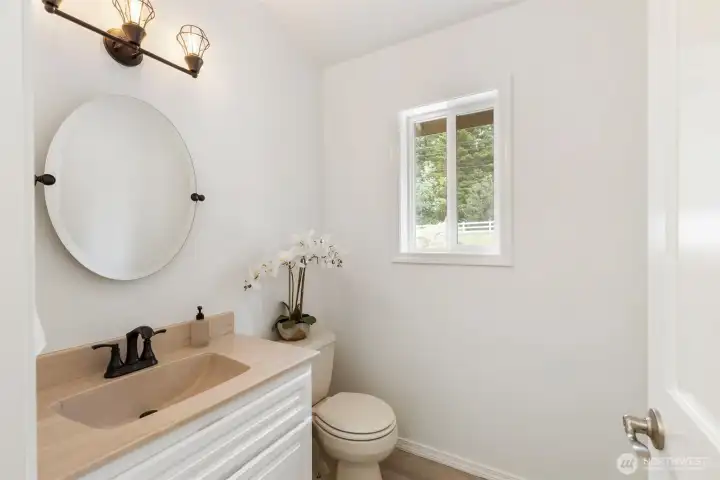 Main-level half bath with elegant finishes, warm lighting, and a bright window view—offering refined convenience for guests and everyday living.