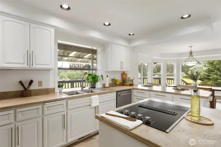 Natural light pours through expansive windows, illuminating the upgraded kitchen with a bright, refined feel. White and elegant cabinetry, generous counter space, and peaceful acreage views create an elegant centerpiece for luxury Kitsap County living